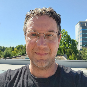 A middle-aged white man with glasses, city trees and buildings in background (Lloyd District, Portland)